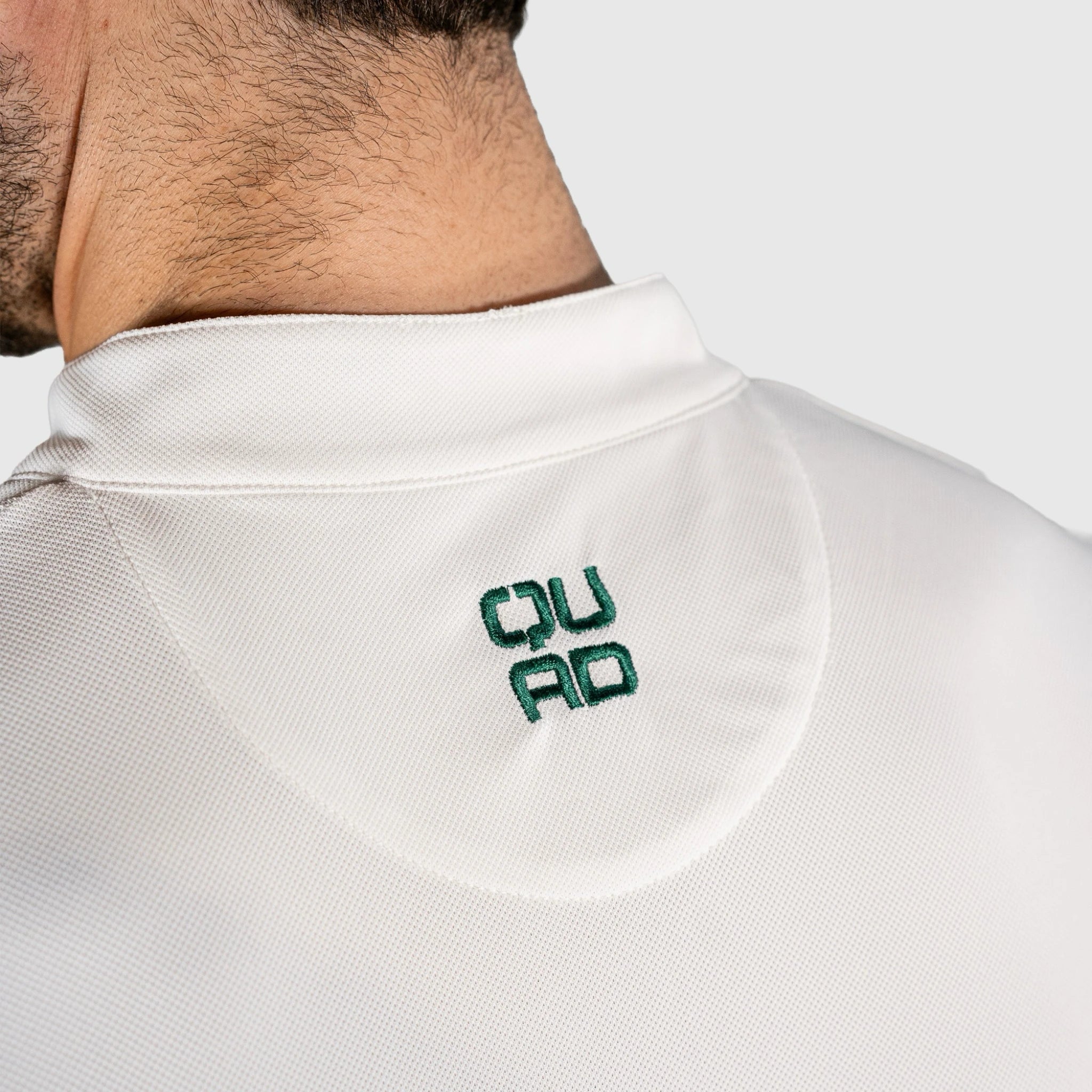 Close-up of a QUAD Padel Polo White with 'QUAD' logo on the collar against a light grey background