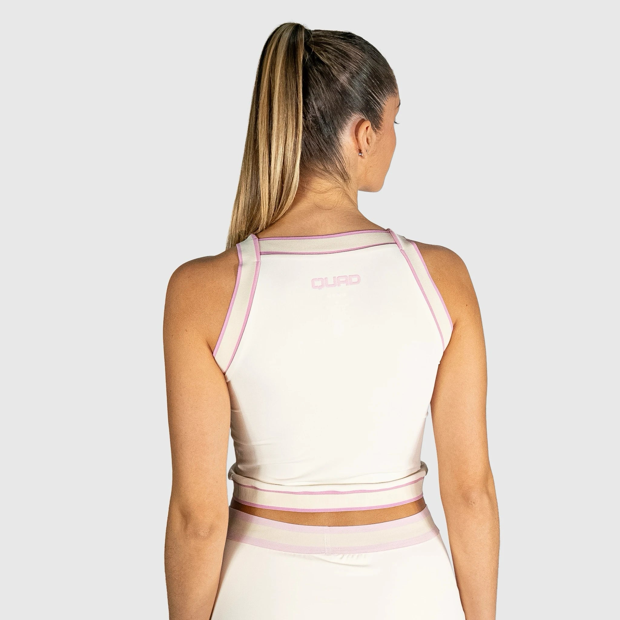 Woman wearing a slice padel top with pink accents on a plain background