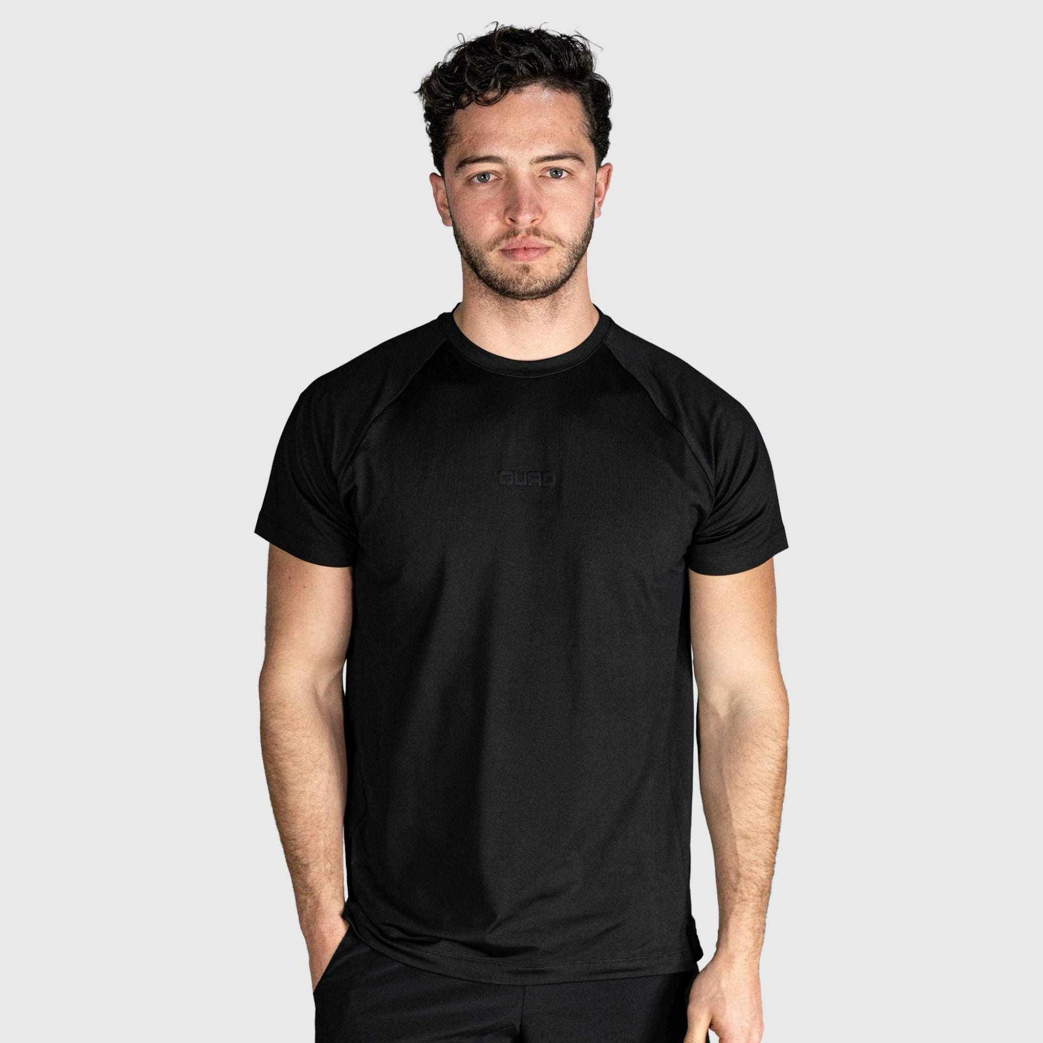 Man wearing a QUAD Ace Padel T shirt black on a light gray background