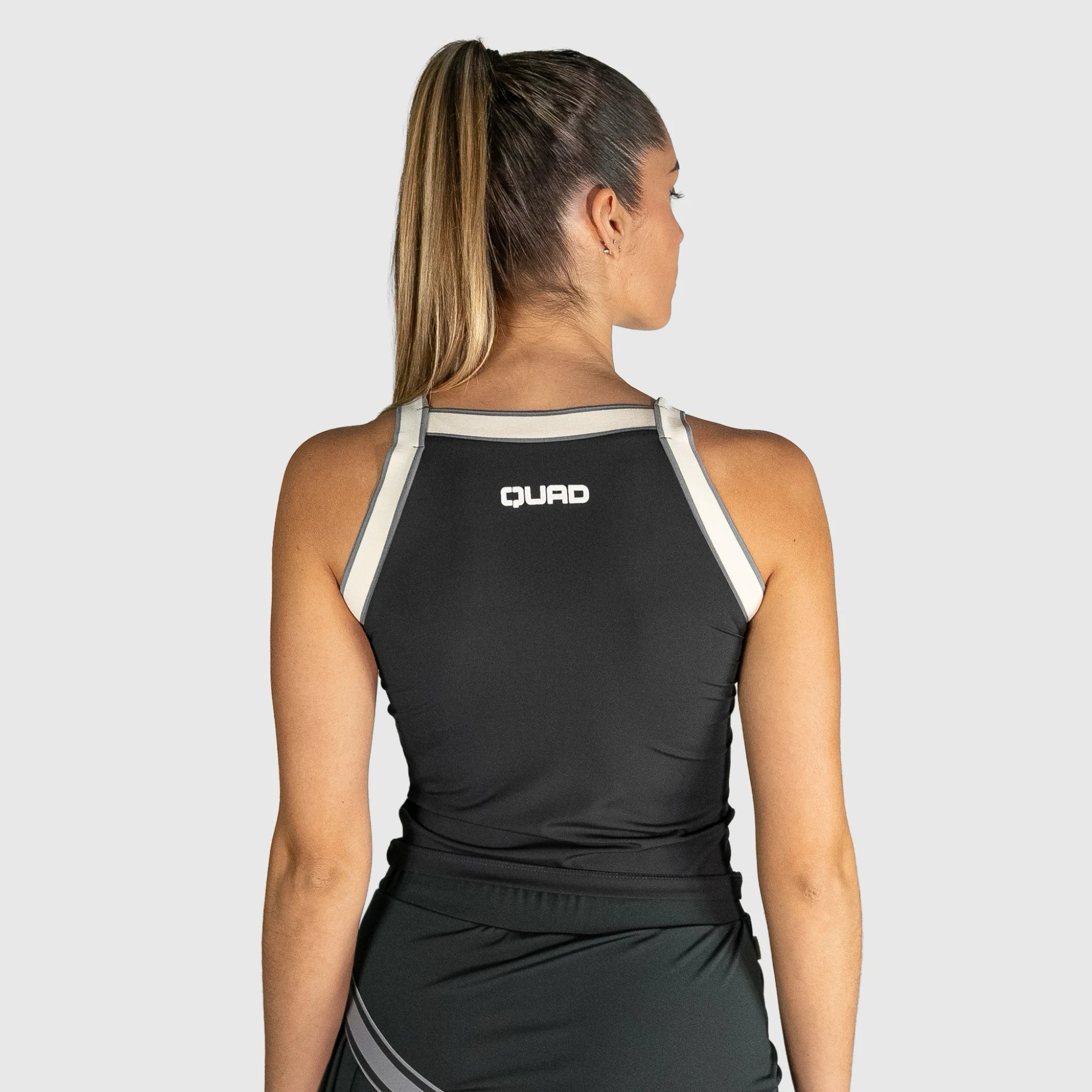 Woman wearing a QUAD Aim Padel Top with 'QUAD' branding on a light grey background