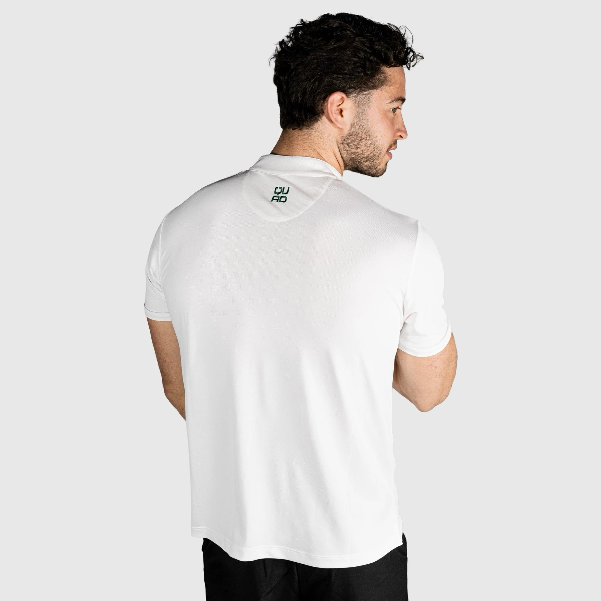 Man wearing a QUAD Padel Polo White with a brand logo on the back against a light grey background