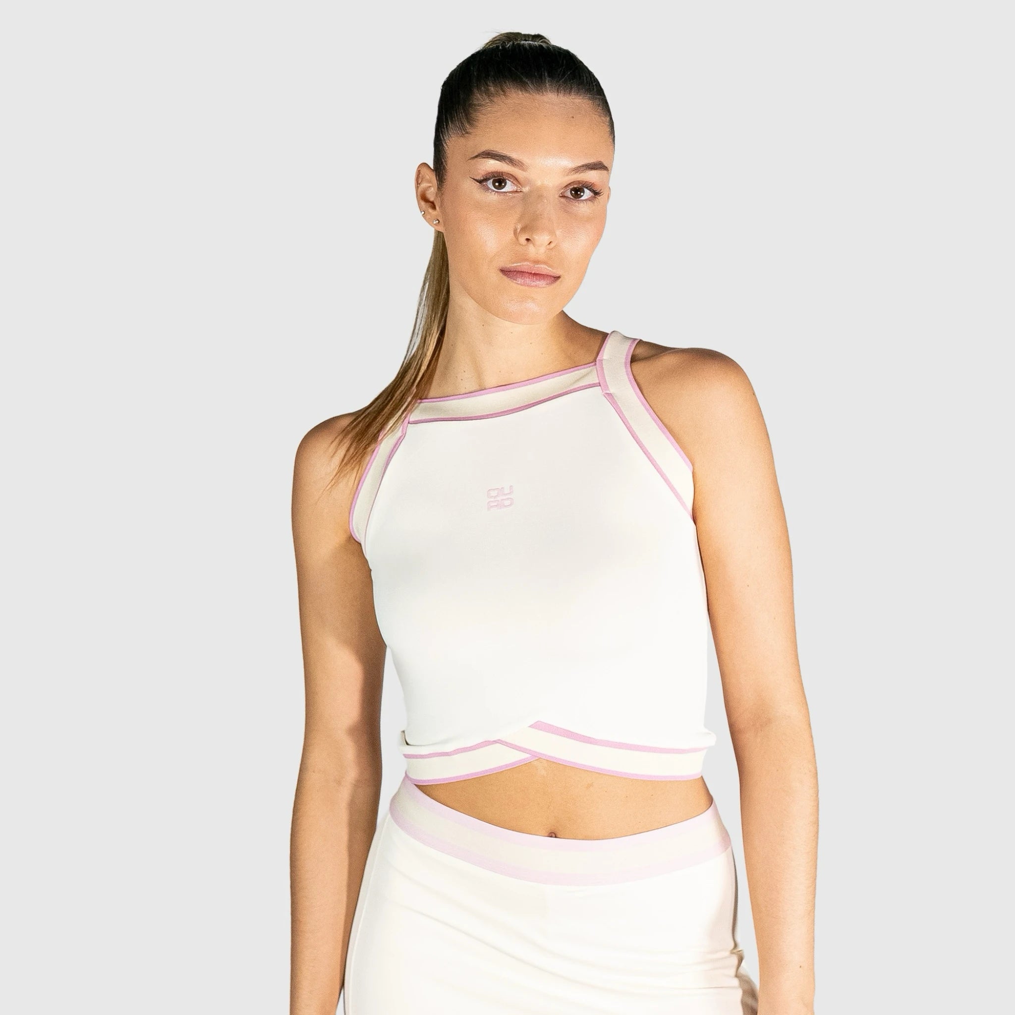 Woman wearing a white slice padel top with pink accents on a light grey background